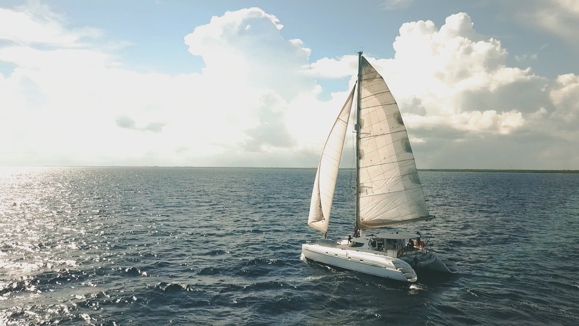 Elegant white catamaran sailing across the clear blue Caribbean waters under a partly cloudy sky